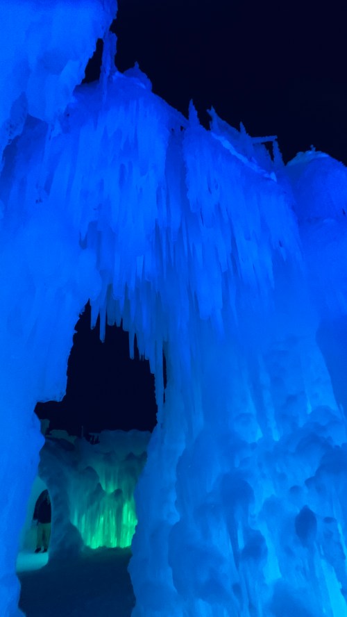 Glowing blue and green ice formations create a magical, cave-like atmosphere in a winter landscape.