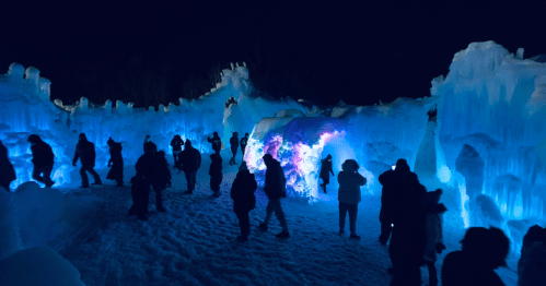 A winter scene with illuminated ice formations and people exploring the icy landscape at night.