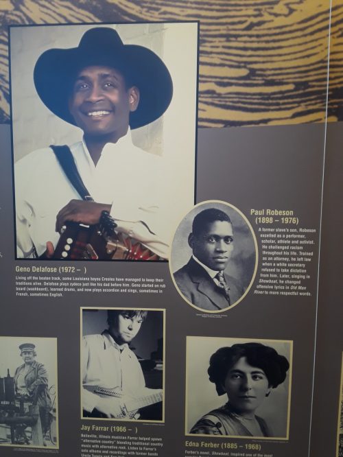 Image features a display with portraits and information about notable figures: Geno Delafose, Paul Robeson, Jay Farnier, and Edna Ferber.