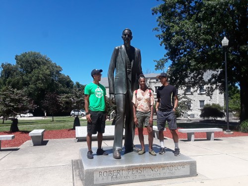 Three people stand beside a large bronze statue of Robert Pershing Wadley in a park setting.