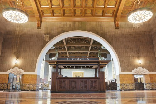 Interior of a grand building featuring an information desk, ornate ceiling, and large arched windows.
