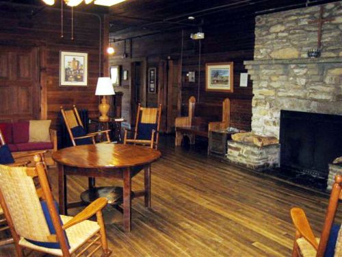 Cozy room with wooden floors, a stone fireplace, rocking chairs, and a round table, creating a warm, inviting atmosphere.