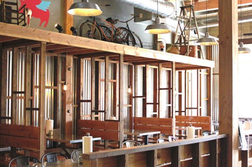 A modern restaurant interior featuring wooden booths, industrial decor, and bicycles hanging from the ceiling.