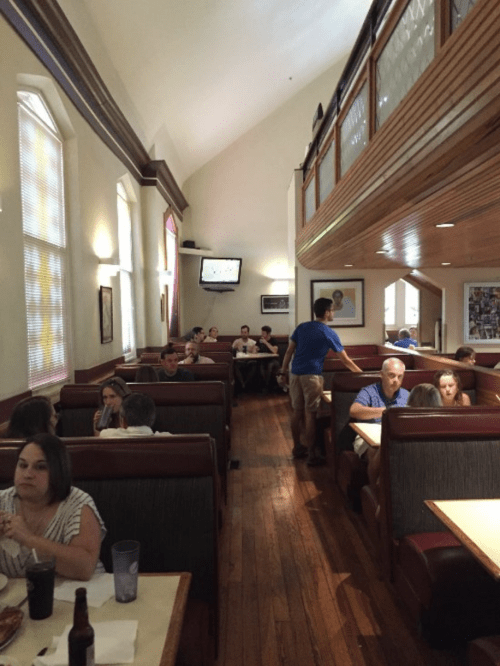 A busy restaurant interior with booths, diners enjoying meals, and a person walking between tables.