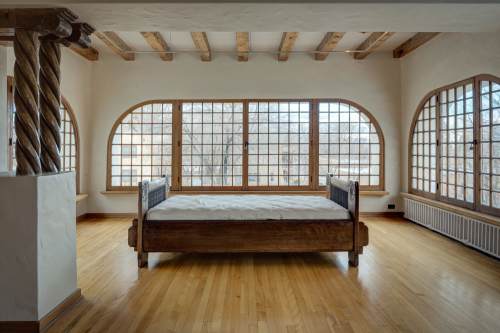 A spacious room with a wooden bed, large arched windows, and wooden beams on the ceiling, featuring a warm, inviting atmosphere.