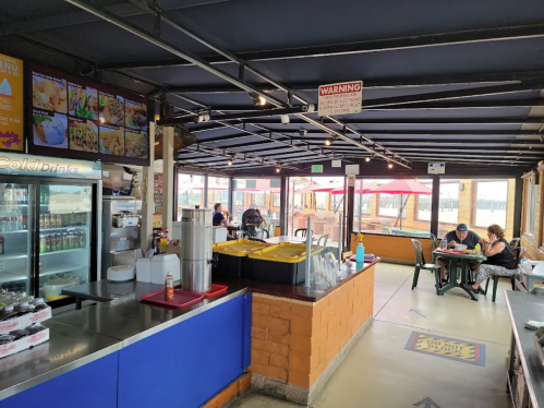 A casual dining area with a counter, menu board, and tables, featuring a bright, open atmosphere and outdoor seating.