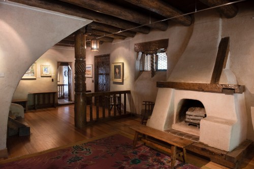 Cozy interior of a rustic room featuring a wooden beam ceiling, a fireplace, and colorful rugs.