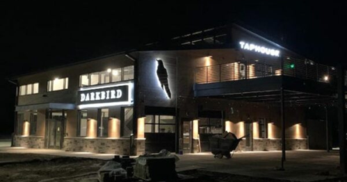 A modern building at night featuring illuminated signs for "Darkbird" and "Taphouse."