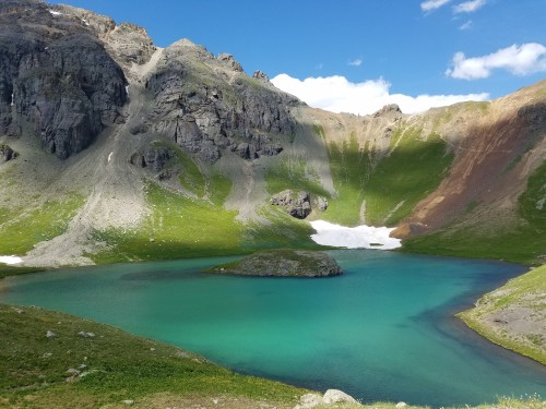 A serene mountain lake surrounded by rocky cliffs and lush green hills under a clear blue sky.