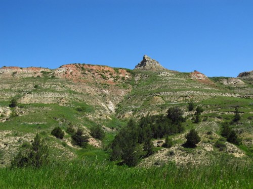 A rugged hillside with colorful rock layers and green vegetation under a clear blue sky.