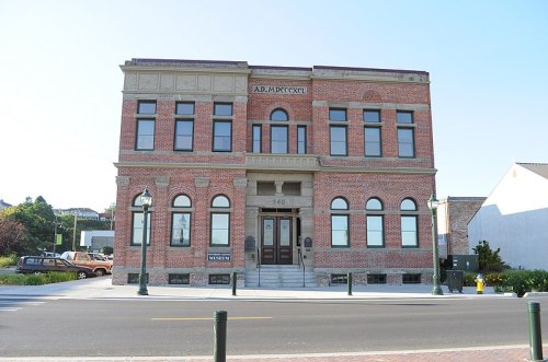 Historic brick building with large windows, featuring the year 1892, located on a street with lampposts and greenery.
