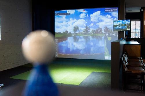 A golf simulator setup with a large screen displaying a scenic course and a small blue golf tee in the foreground.