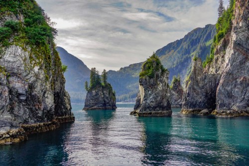 A serene landscape featuring rocky islands surrounded by calm turquoise waters and lush green mountains in the background.