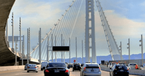 Traffic on a bridge with a modern design, featuring tall cables and a clear blue sky in the background.