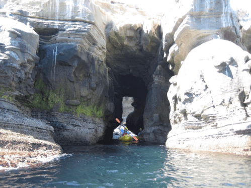 A kayaker navigates through a narrow rock formation with water reflecting sunlight.