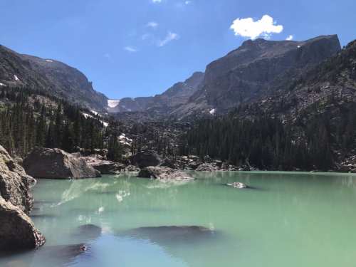 A serene mountain landscape with a turquoise lake, surrounded by rocky cliffs and lush green trees under a clear blue sky.