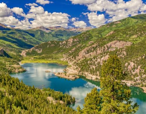A serene mountain landscape featuring a clear blue lake surrounded by lush greenery and dramatic clouds.