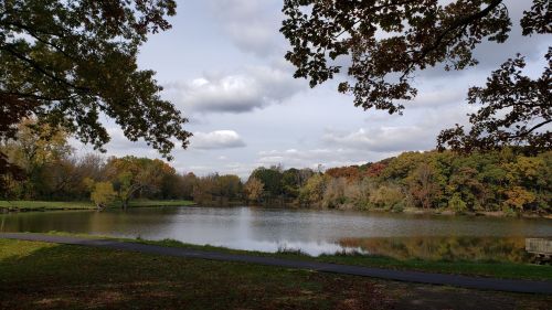 A serene lake surrounded by autumn foliage and cloudy skies, reflecting the trees in the calm water.