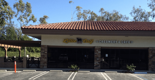 Exterior of Little Calf Creamery & Café, featuring a tiled roof and large windows, surrounded by trees and a parking lot.