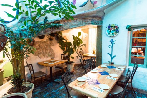Cozy restaurant interior with wooden tables, plants, and colorful wall art, creating a warm and inviting atmosphere.