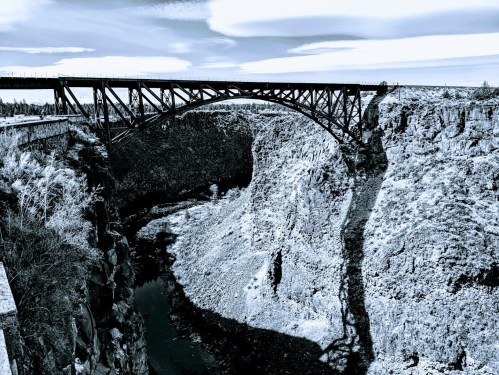 A black and white image of a large bridge spanning a deep canyon with a river below.
