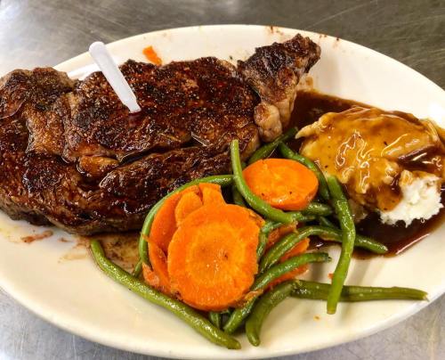 A plate featuring a grilled steak, mashed potatoes with gravy, and a side of carrots and green beans.
