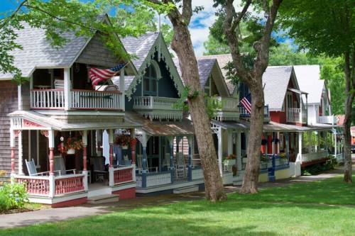Colorful Victorian-style houses with porches, surrounded by trees and greenery, some displaying American flags.