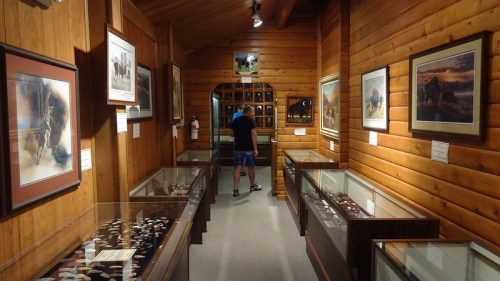 A person explores a wooden museum hallway lined with framed artwork and display cases.