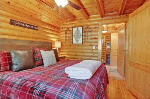 Cozy log cabin bedroom with a plaid bedspread, wooden walls, and warm lighting. A towel is neatly rolled on the bed.