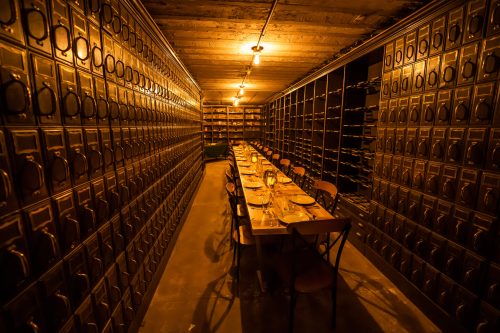 A dimly lit room with a long wooden table surrounded by rows of metal storage boxes.