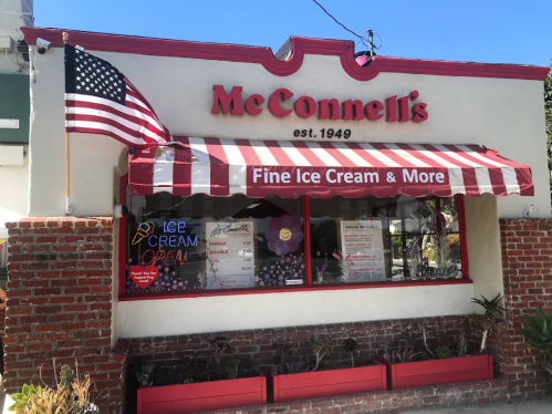A charming ice cream shop with a red and white striped awning, featuring a flag and a sign that reads "Fine Ice Cream & More."