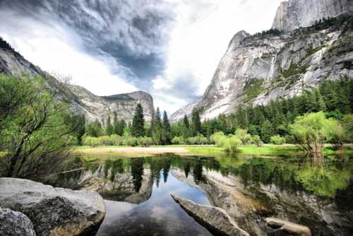 A serene landscape featuring mountains, lush trees, and a reflective lake under a cloudy sky.