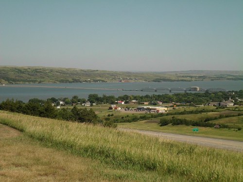 A scenic view of a river valley with a bridge, green hills, and a small town in the foreground under a clear sky.