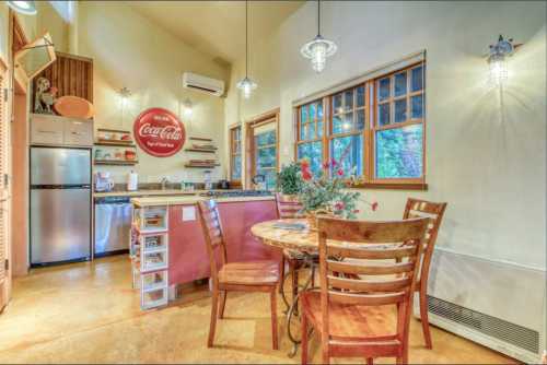 Cozy kitchen with a round table, wooden chairs, and a Coca-Cola sign, featuring warm lighting and a modern fridge.