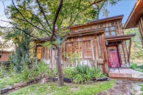 A rustic wooden house surrounded by greenery, featuring large windows and a welcoming front porch.