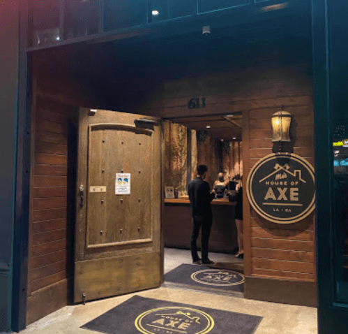 Entrance to House of Axe, featuring a wooden door and a sign, with a person standing inside. Warm, inviting atmosphere.