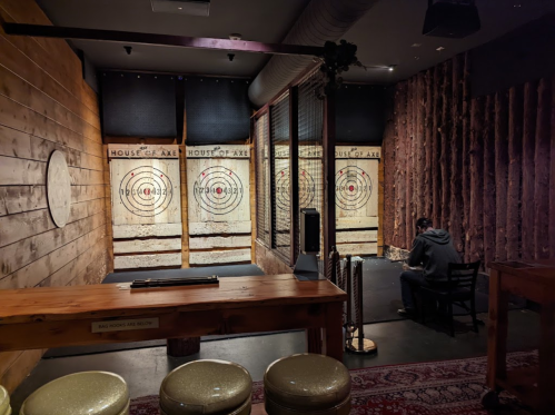 A cozy axe-throwing venue with wooden walls, targets, and a seating area. A person sits quietly in the background.