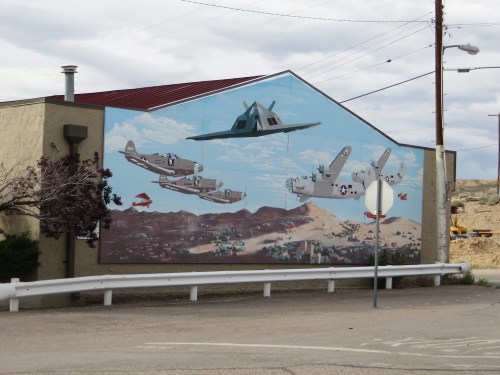 Mural on a building depicting military aircraft flying over a landscape with clouds and mountains.
