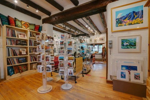 Art gallery interior featuring shelves of books, artwork, and a display of greeting cards under wooden beams.