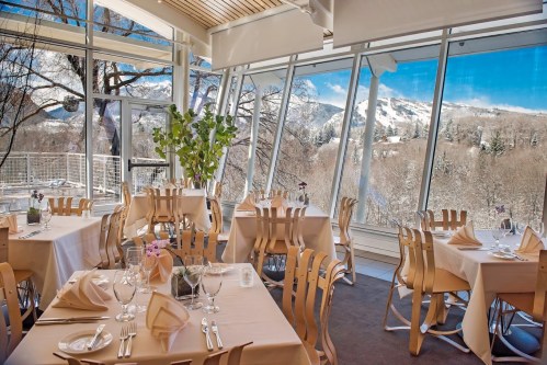 A modern restaurant with large windows showcasing a snowy mountain view, featuring elegantly set tables.