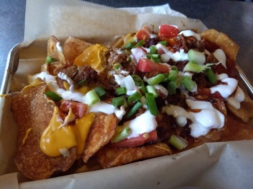 A tray of loaded nachos topped with cheese, beef, tomatoes, green onions, and sour cream on a bed of tortilla chips.