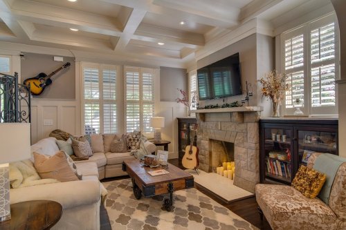 Cozy living room with a sectional sofa, coffee table, fireplace, and guitar on the wall, featuring warm lighting and decor.