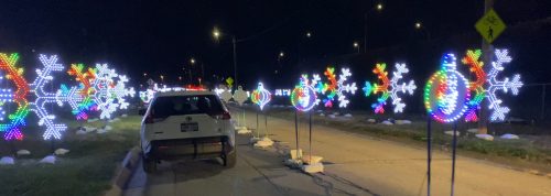 A car parked on a road lined with colorful, illuminated snowflakes and ornaments during a nighttime display.