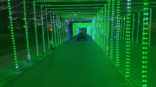 A pathway illuminated by vibrant green lights, creating a tunnel effect with a vehicle in the center.