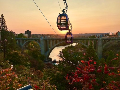 A scenic view of a bridge at sunset, with gondolas in the foreground and colorful foliage along the riverbank.