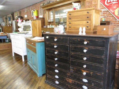 A vintage furniture display featuring various wooden cabinets and drawers in a rustic shop setting.