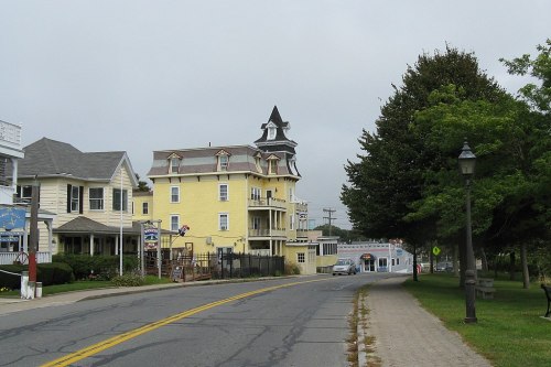 A quiet street lined with charming houses, featuring a distinctive yellow building with a tower and trees along the sidewalk.