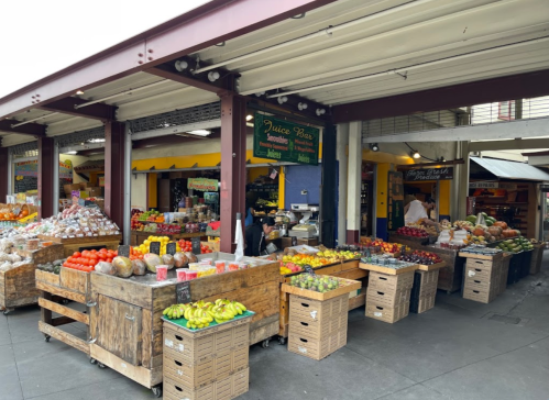 A vibrant market scene with wooden stalls filled with various fruits and vegetables under a covered area.