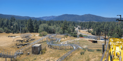 A scenic view of a roller coaster track winding through a forested area with mountains in the background.