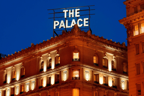 The illuminated facade of The Palace hotel at night, featuring a prominent rooftop sign.